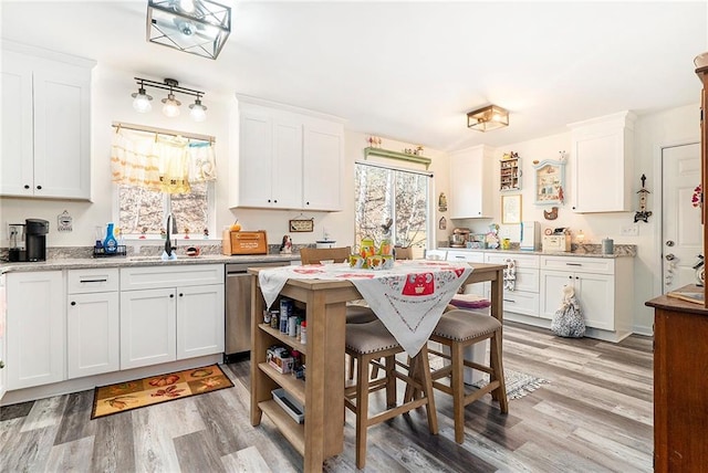 kitchen with sink, dishwasher, white cabinetry, light stone counters, and a kitchen bar