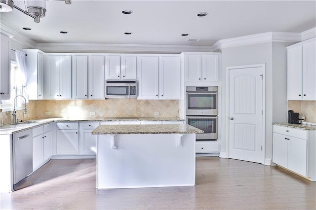 kitchen with sink, white cabinetry, a kitchen island, stainless steel appliances, and light stone countertops