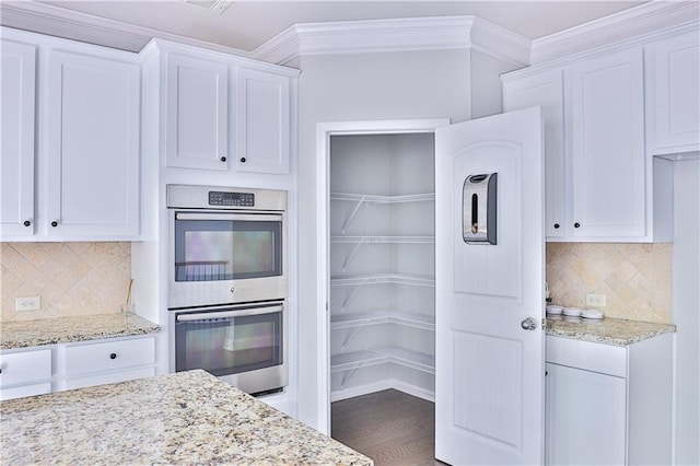 kitchen with stainless steel double oven, dark hardwood / wood-style floors, light stone countertops, and white cabinets