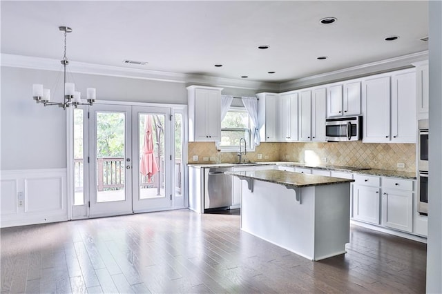 kitchen with stainless steel appliances, a kitchen island, white cabinets, and dark stone counters