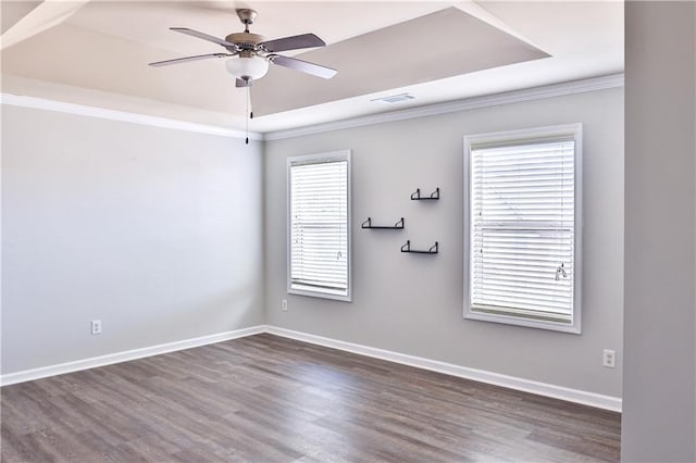 spare room with dark wood-type flooring, ceiling fan, ornamental molding, and a raised ceiling