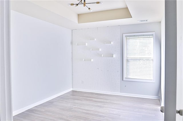 empty room featuring a notable chandelier, light wood-type flooring, and a tray ceiling