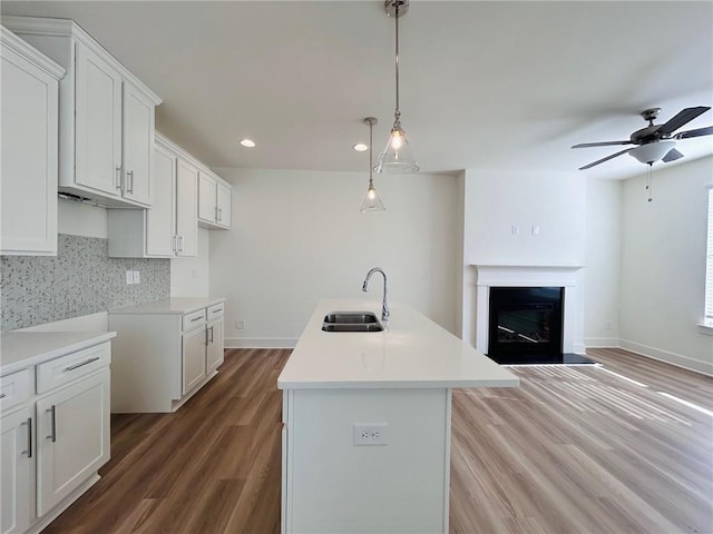 kitchen with sink, white cabinetry, backsplash, an island with sink, and decorative light fixtures