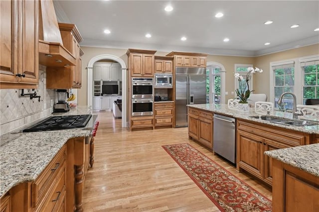 kitchen featuring light stone countertops, built in appliances, decorative backsplash, sink, and custom range hood