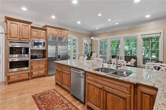 kitchen with built in appliances, light hardwood / wood-style floors, sink, ornamental molding, and light stone counters