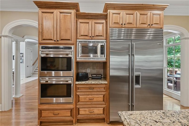 kitchen featuring crown molding, light stone counters, built in appliances, and decorative columns