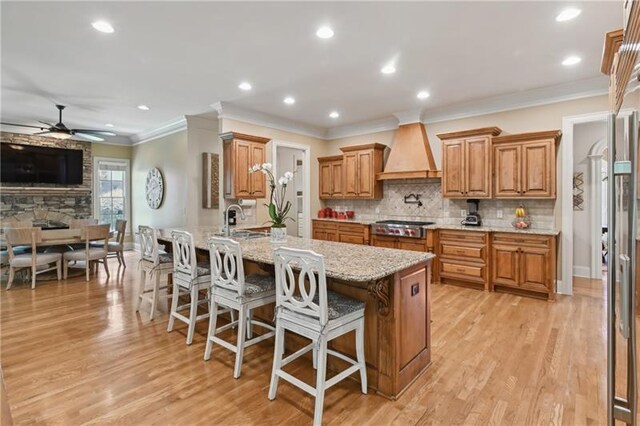 kitchen featuring custom exhaust hood, a breakfast bar area, ceiling fan, light stone countertops, and sink