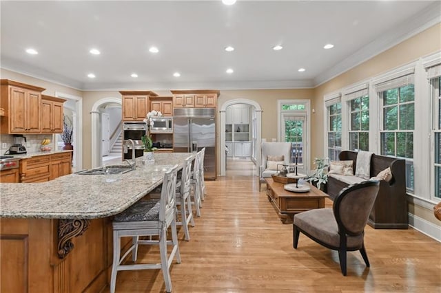 kitchen featuring light stone countertops, a spacious island, built in appliances, tasteful backsplash, and a breakfast bar