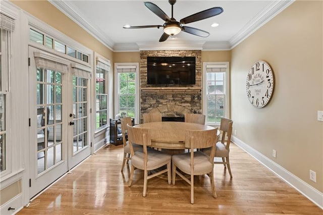 dining room with ceiling fan, light wood-type flooring, a stone fireplace, ornamental molding, and french doors