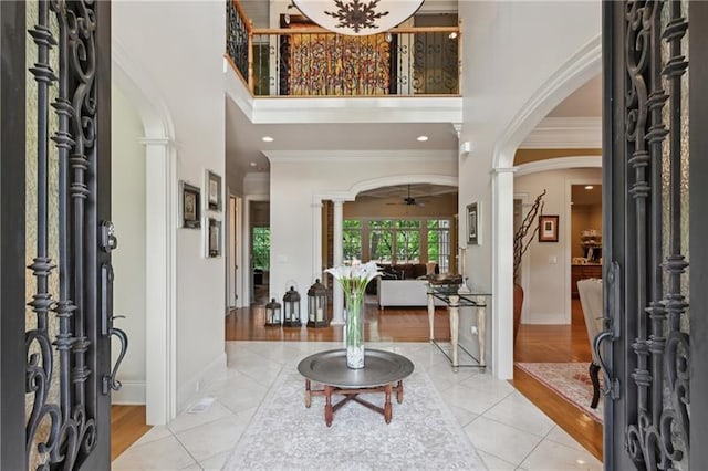 foyer with ceiling fan, light tile patterned floors, crown molding, and a towering ceiling