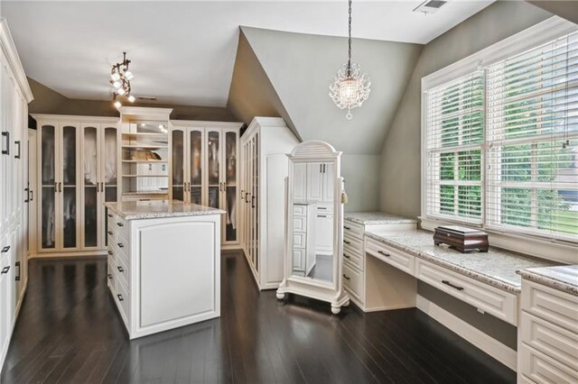 kitchen with decorative light fixtures, dark hardwood / wood-style flooring, lofted ceiling, light stone countertops, and a center island