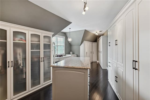 kitchen with light stone countertops, white cabinets, a kitchen island, hanging light fixtures, and vaulted ceiling