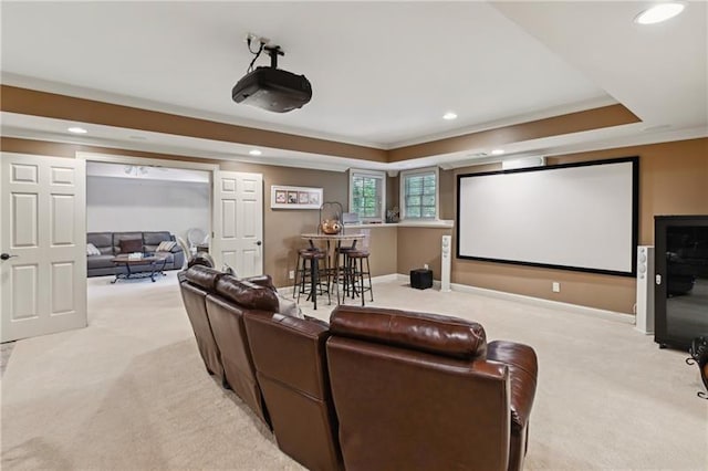 carpeted home theater room with a raised ceiling and ornamental molding