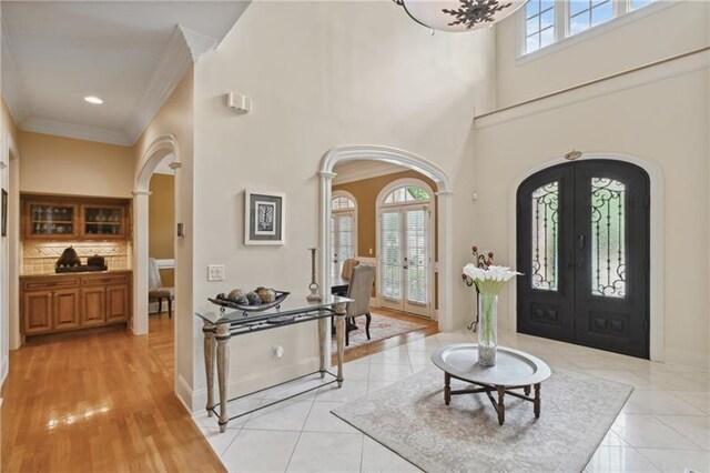 foyer entrance with a towering ceiling, light tile patterned flooring, ornamental molding, and french doors