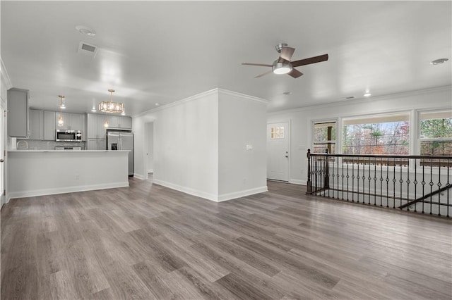 unfurnished living room featuring ceiling fan with notable chandelier, baseboards, wood finished floors, visible vents, and ornamental molding