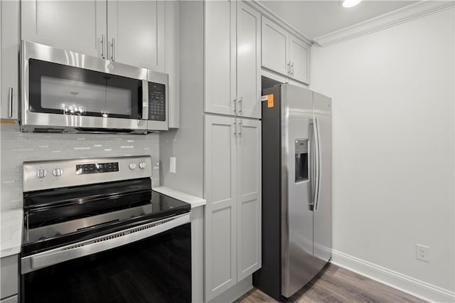 kitchen featuring backsplash, crown molding, wood finished floors, baseboards, and stainless steel appliances