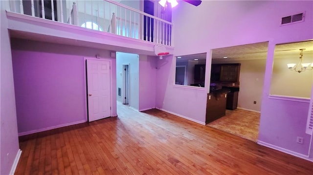 empty room featuring ceiling fan with notable chandelier, a high ceiling, and hardwood / wood-style flooring