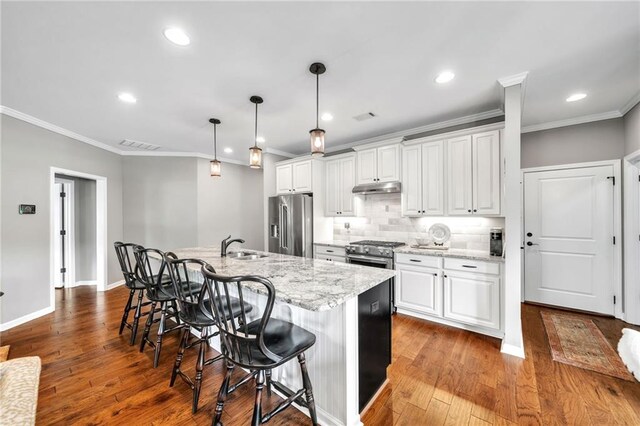 kitchen featuring appliances with stainless steel finishes, light stone counters, wood-type flooring, white cabinets, and an island with sink