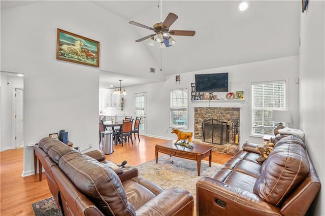 living room with light wood-style floors, a fireplace, high vaulted ceiling, and a ceiling fan