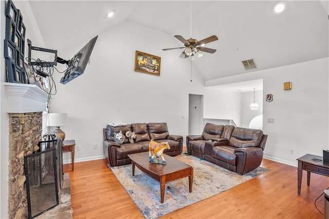 living area featuring a fireplace, visible vents, ceiling fan, wood finished floors, and high vaulted ceiling