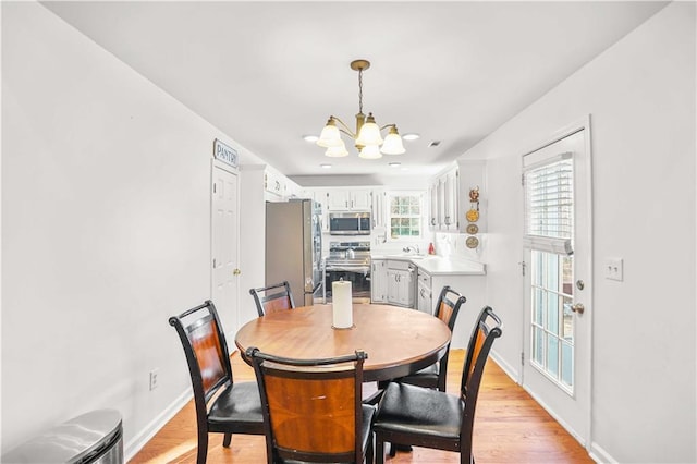 dining area featuring light wood-style flooring, baseboards, and a notable chandelier