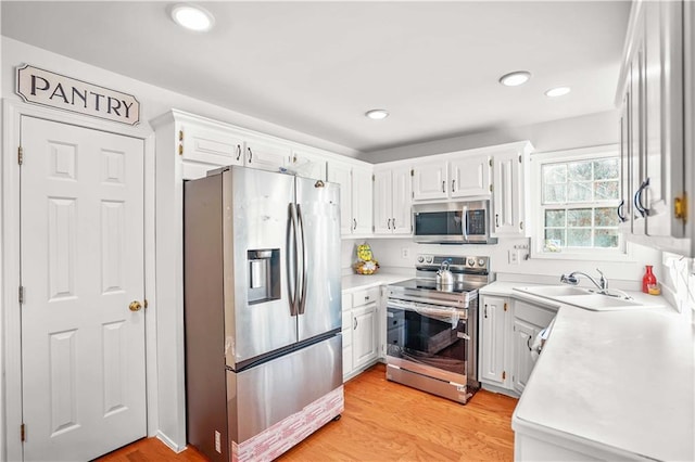 kitchen featuring appliances with stainless steel finishes, white cabinets, light countertops, and a sink