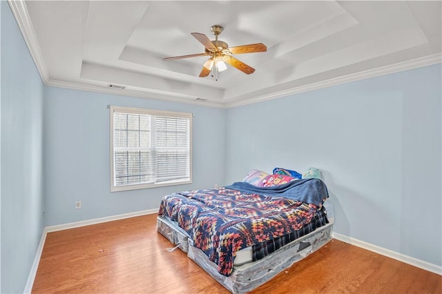 bedroom with crown molding, a raised ceiling, a ceiling fan, wood finished floors, and baseboards