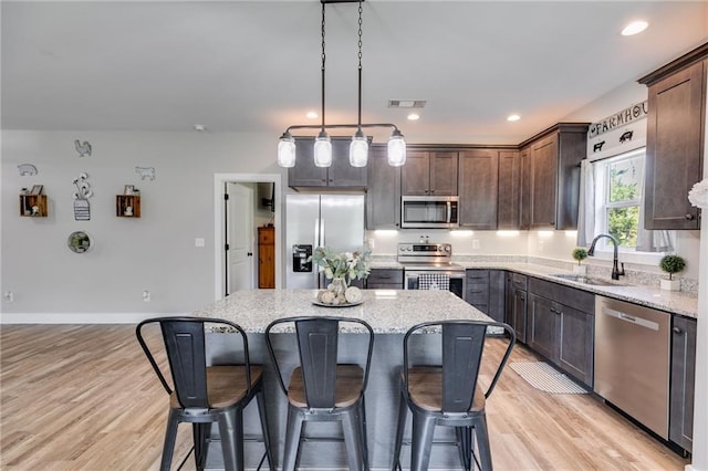 kitchen with sink, hanging light fixtures, dark brown cabinets, appliances with stainless steel finishes, and a kitchen island