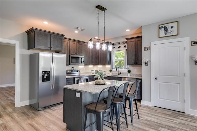 kitchen featuring dark brown cabinetry, sink, a center island, hanging light fixtures, and stainless steel appliances