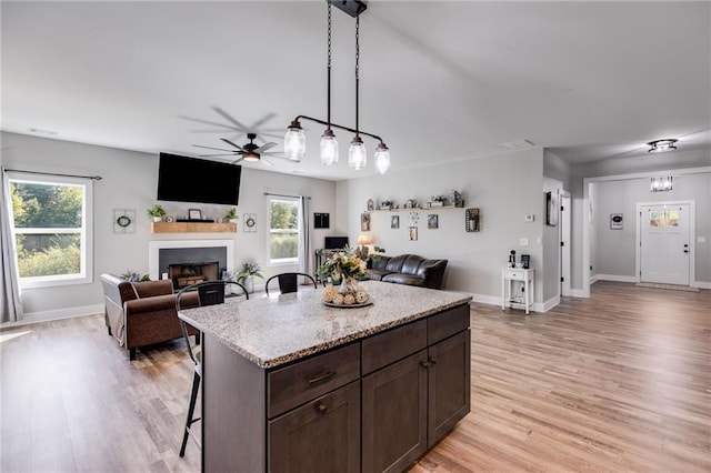 kitchen featuring a kitchen island, a kitchen breakfast bar, hanging light fixtures, dark brown cabinetry, and light hardwood / wood-style flooring