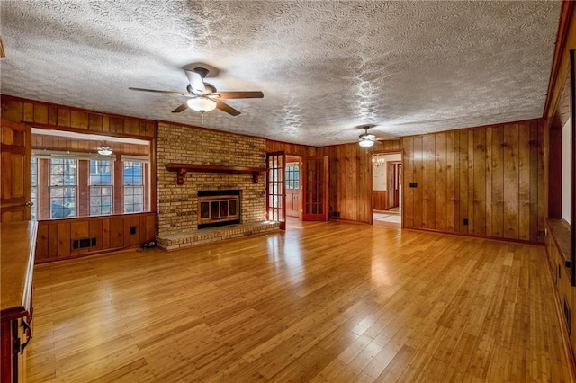 unfurnished living room featuring ceiling fan, a fireplace, and wood walls