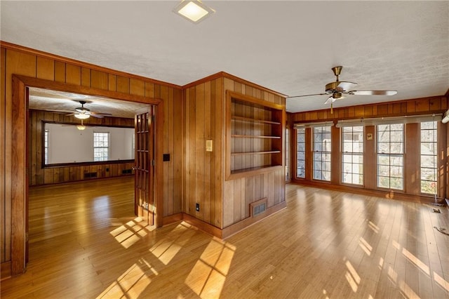 unfurnished living room with ornamental molding, ceiling fan, built in features, and light hardwood / wood-style floors