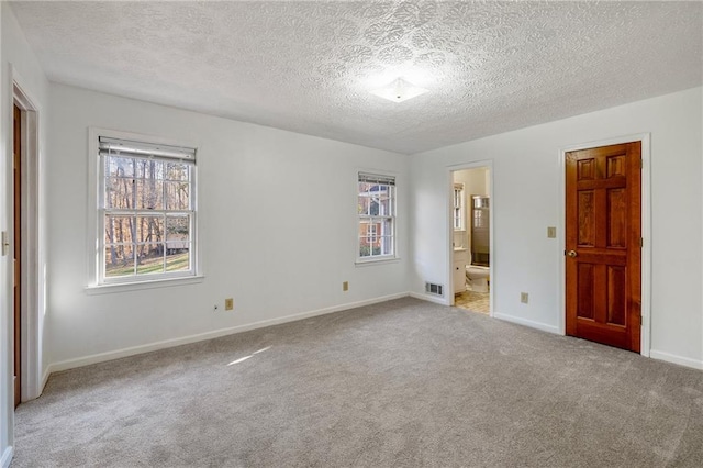 unfurnished bedroom featuring light carpet, connected bathroom, and a textured ceiling