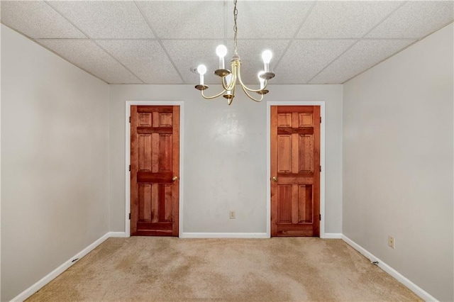 carpeted spare room featuring a drop ceiling and a notable chandelier