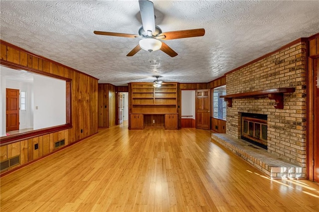 unfurnished living room featuring ornamental molding, wooden walls, a brick fireplace, and a textured ceiling