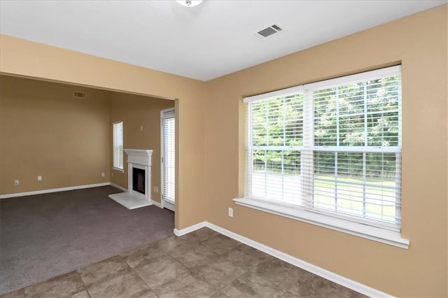 unfurnished living room with visible vents, carpet floors, baseboards, and a fireplace with raised hearth