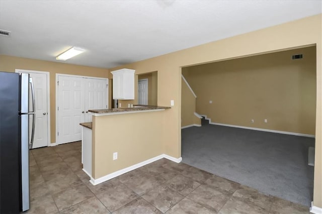 kitchen with visible vents, freestanding refrigerator, white cabinets, carpet flooring, and baseboards