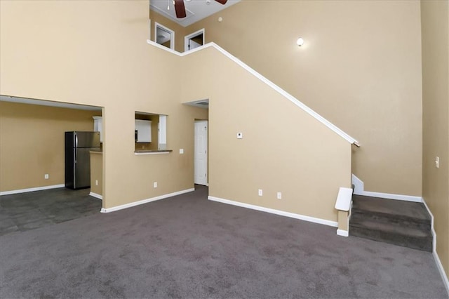 unfurnished living room with baseboards, a high ceiling, ceiling fan, and carpet flooring