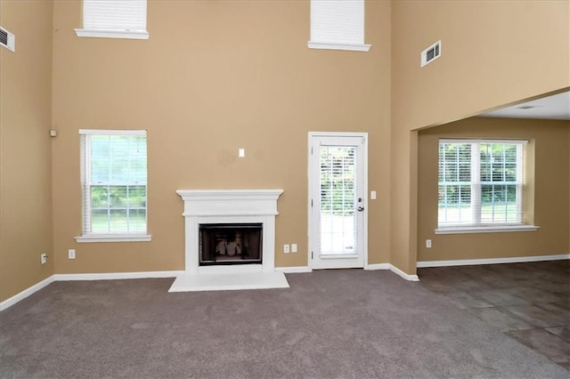 unfurnished living room featuring visible vents, a fireplace with raised hearth, a healthy amount of sunlight, and dark colored carpet