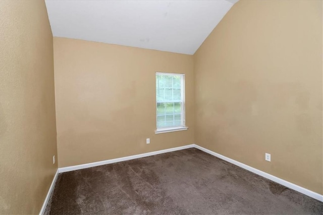 empty room with baseboards, lofted ceiling, and dark colored carpet