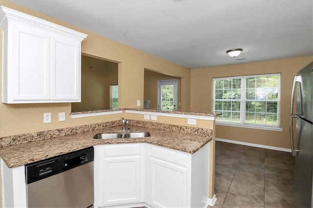 kitchen featuring light stone counters, appliances with stainless steel finishes, a peninsula, white cabinets, and a sink