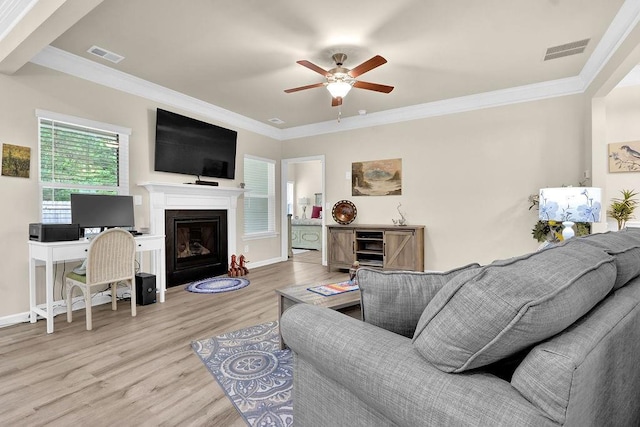 living room with wood finished floors, a ceiling fan, ornamental molding, baseboards, and a glass covered fireplace