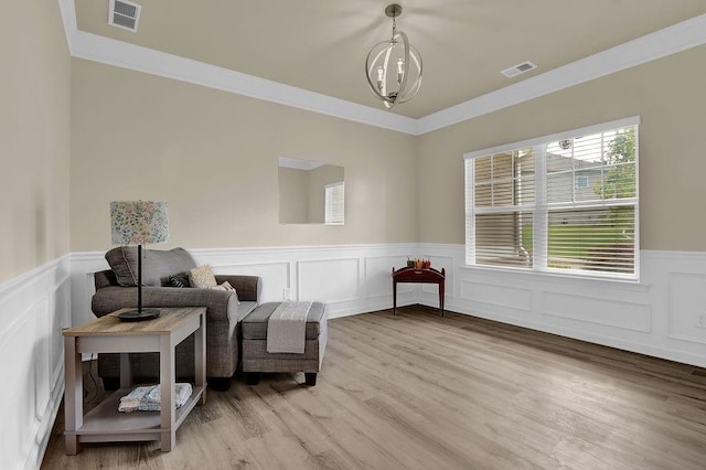 sitting room featuring wainscoting, ornamental molding, light wood-type flooring, and a decorative wall