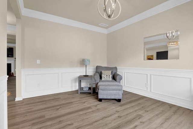 living area featuring a chandelier, ornamental molding, wood finished floors, wainscoting, and a fireplace