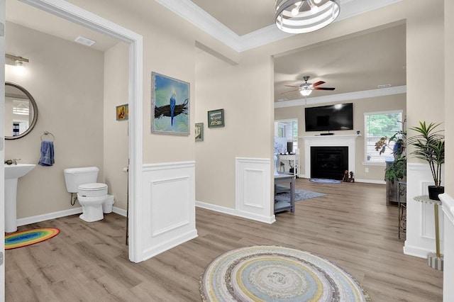 living room featuring crown molding, ceiling fan, light wood-style floors, a fireplace, and baseboards