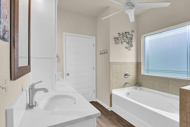 full bath featuring wood finished floors, a ceiling fan, a garden tub, vanity, and baseboards