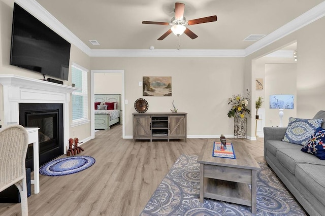 living room featuring wood finished floors, ceiling fan, ornamental molding, a glass covered fireplace, and baseboards