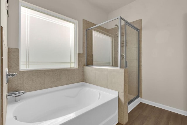 full bathroom featuring a stall shower, a bath, wood finished floors, and baseboards