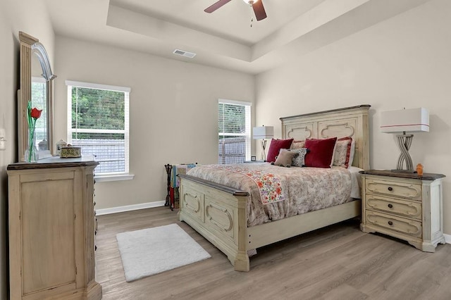 bedroom with light wood finished floors, a raised ceiling, baseboards, and a ceiling fan