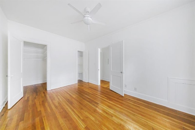 unfurnished bedroom featuring a ceiling fan, two closets, light wood-style flooring, and baseboards